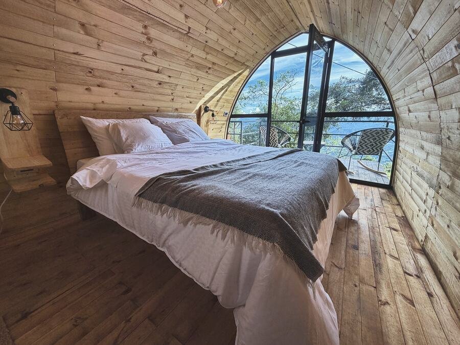 Cama queen con manta gris y ventanal hacia la terraza