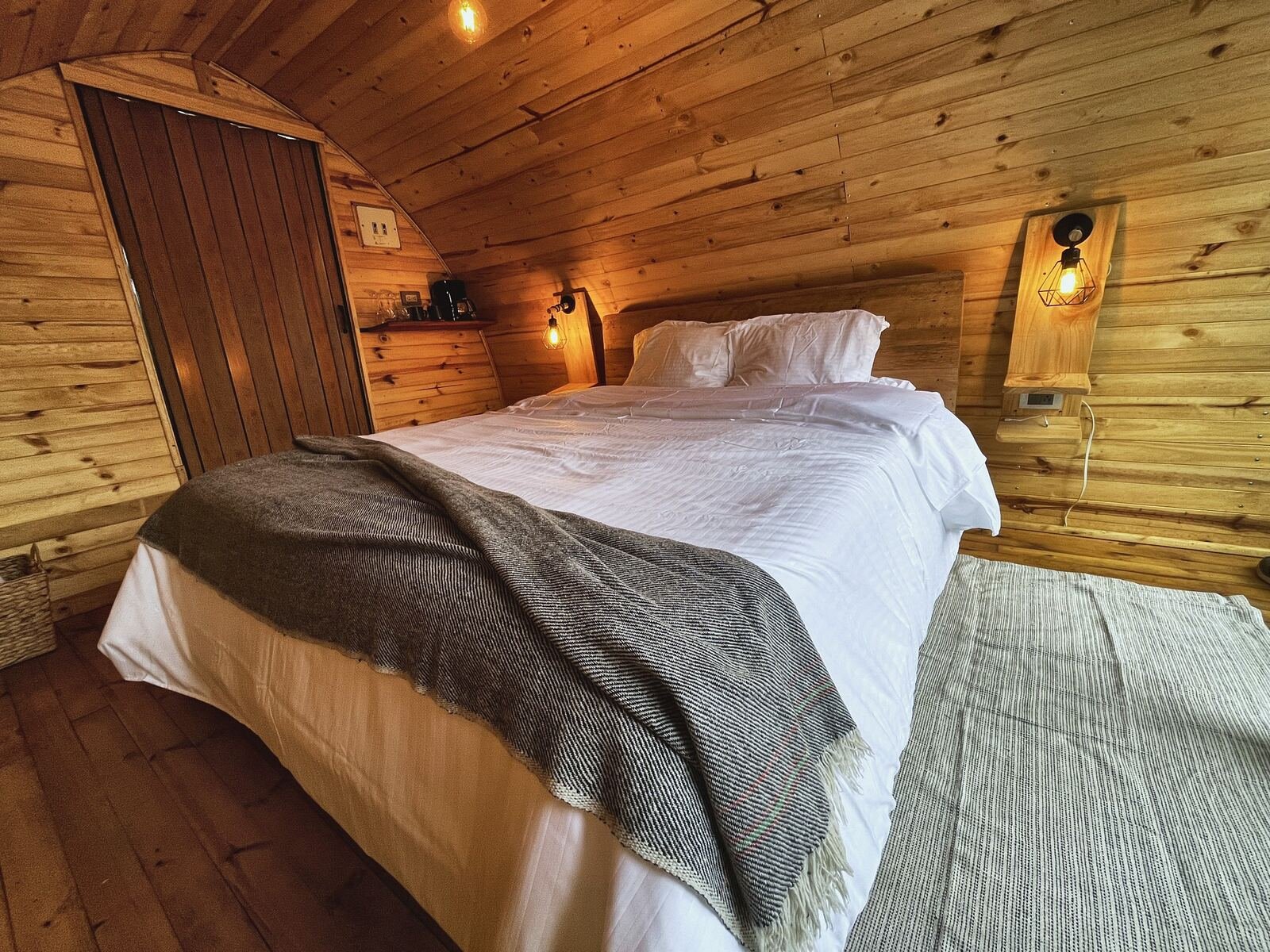 La cabaña de noche, con luz cálida sobre la cama