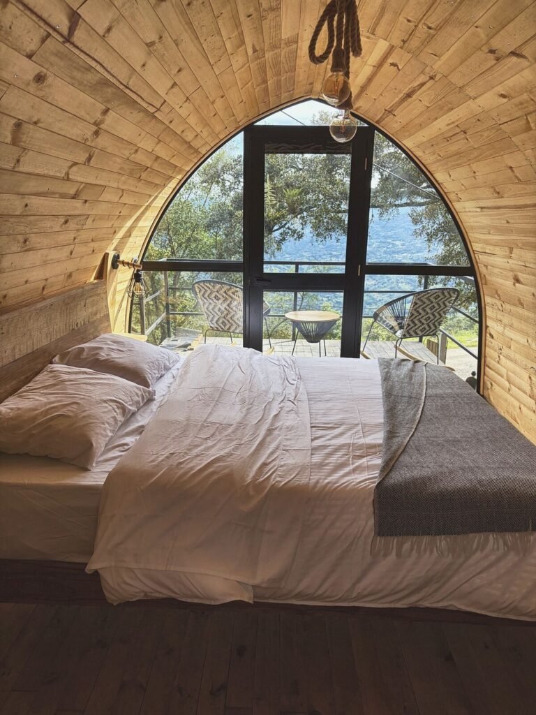 Cama con ropa blanca y manta gris frente al ventanal en arco