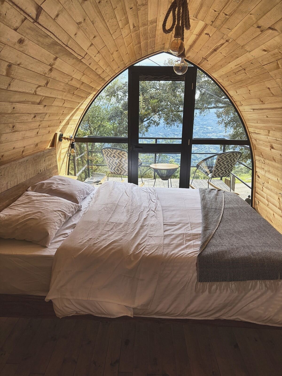 Cama con ropa blanca y manta gris frente al ventanal en arco